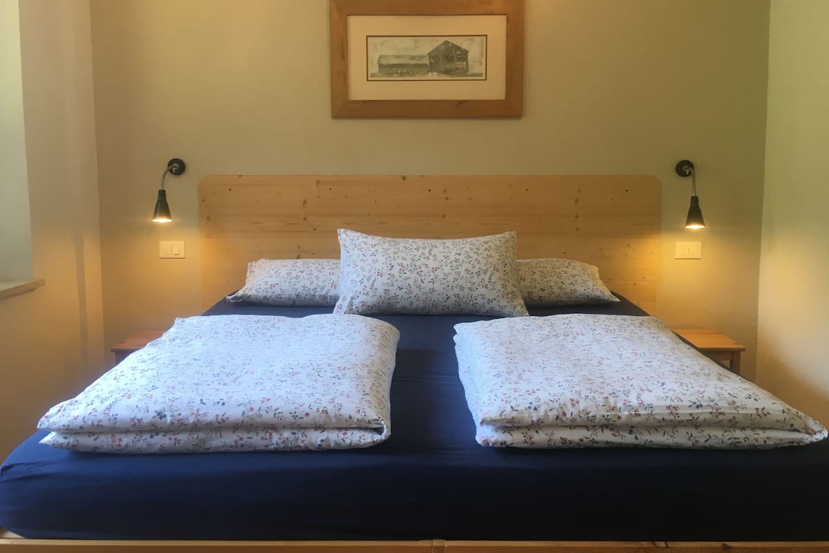 A bed with floral bedding, two bedside lamps, and a framed picture on the wall.