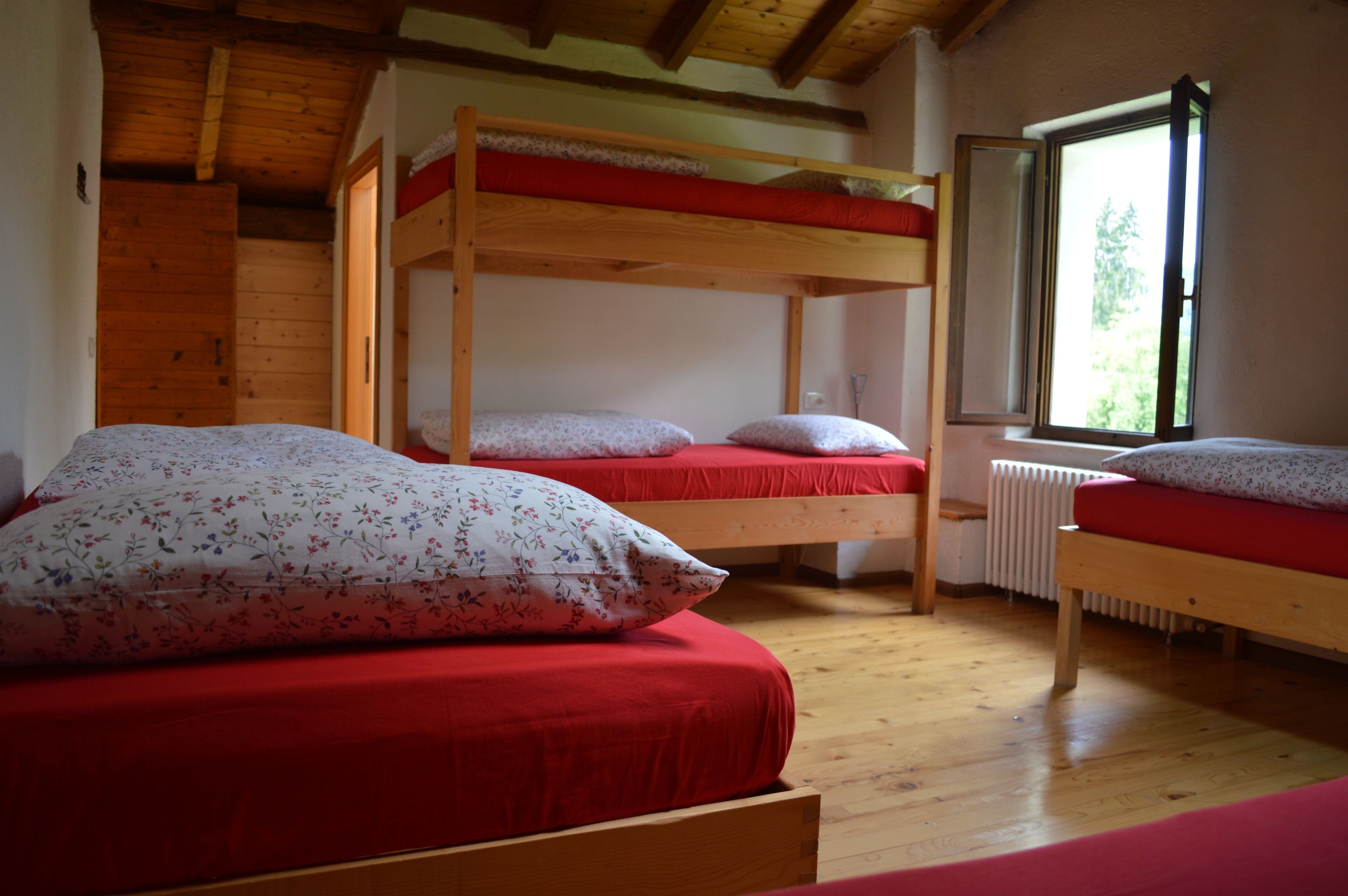 A room with two bunk beds, a window with a view of greenery, and a radiator.