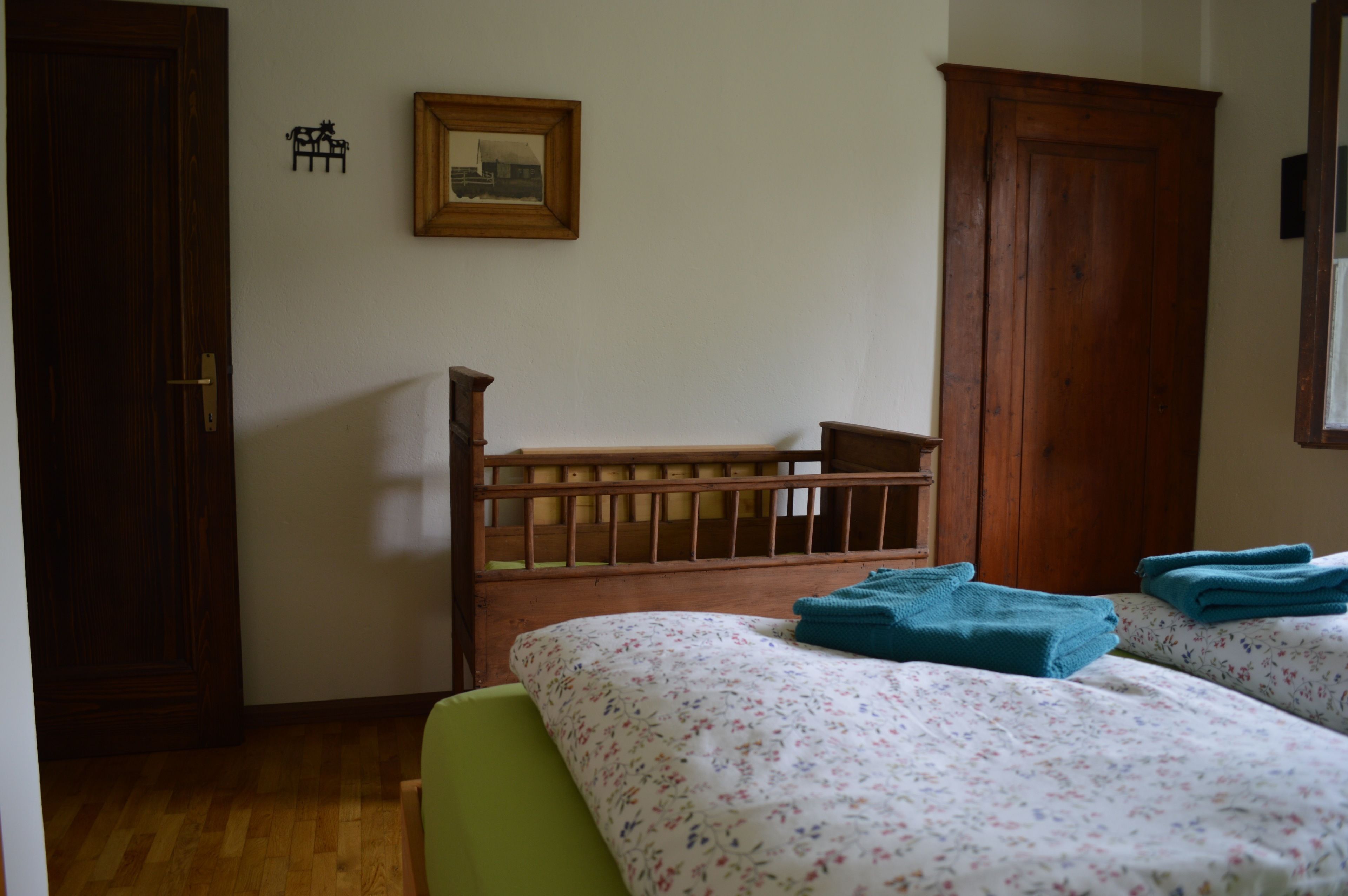 Una habitación con una cama de madera, una silla verde, un armario de madera y un cuadro enmarcado en la pared.