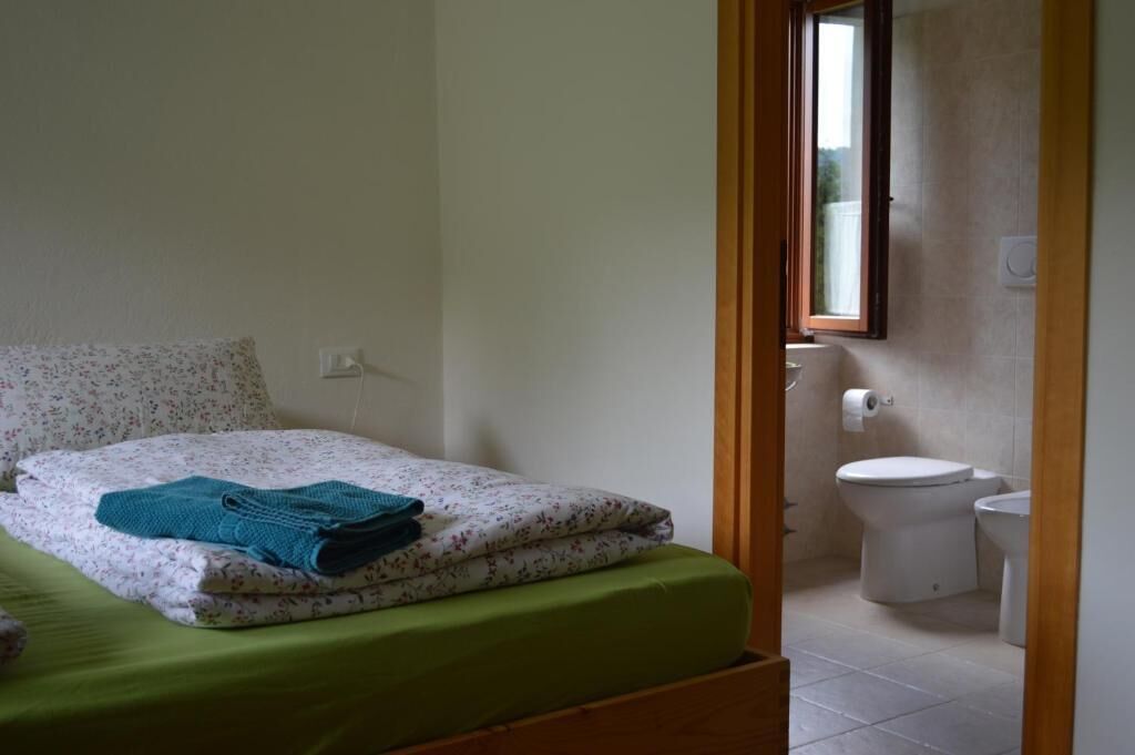 A bedroom with a bed, a green bedspread, a window, and a bathroom with a toilet and sink.