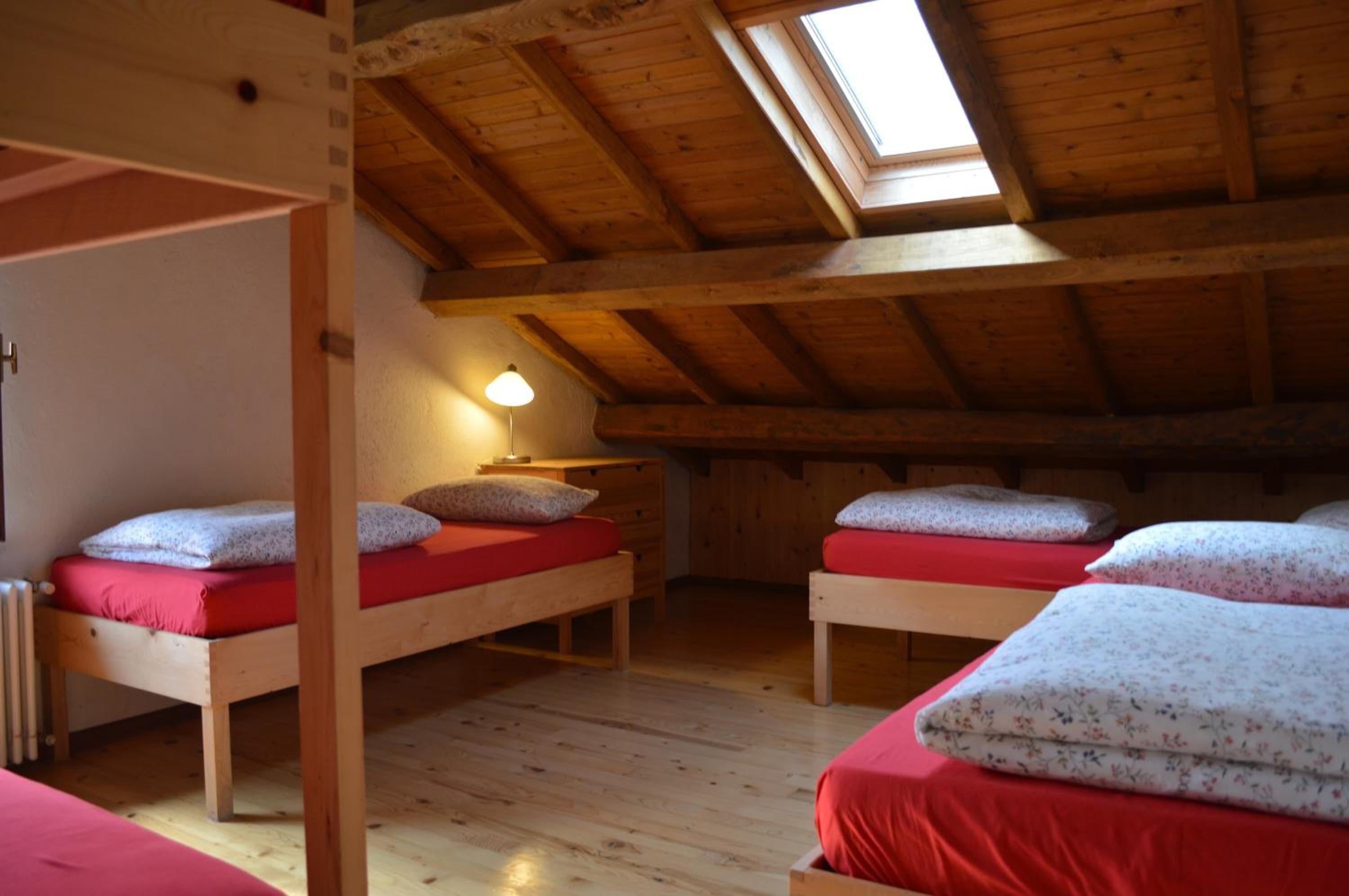 A cozy attic bedroom with wooden beams, two bunk beds, a skylight, and a single bedside table with a lamp.