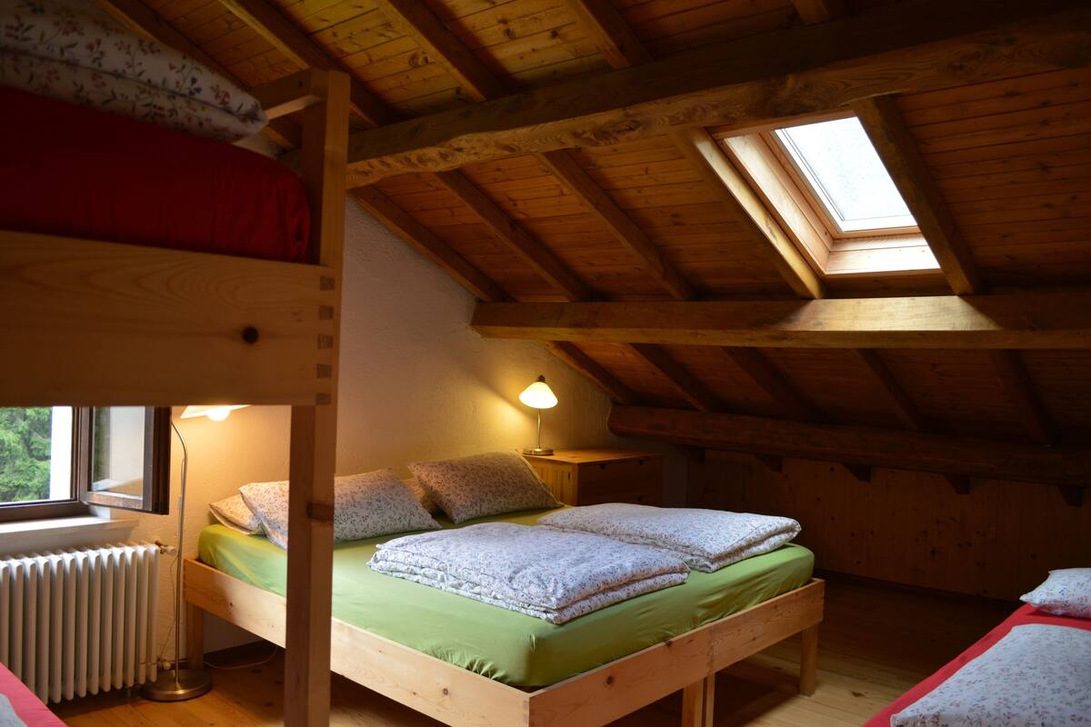 A wooden room with a bunk bed, a single bed, a skylight, a radiator, and a bedside lamp.