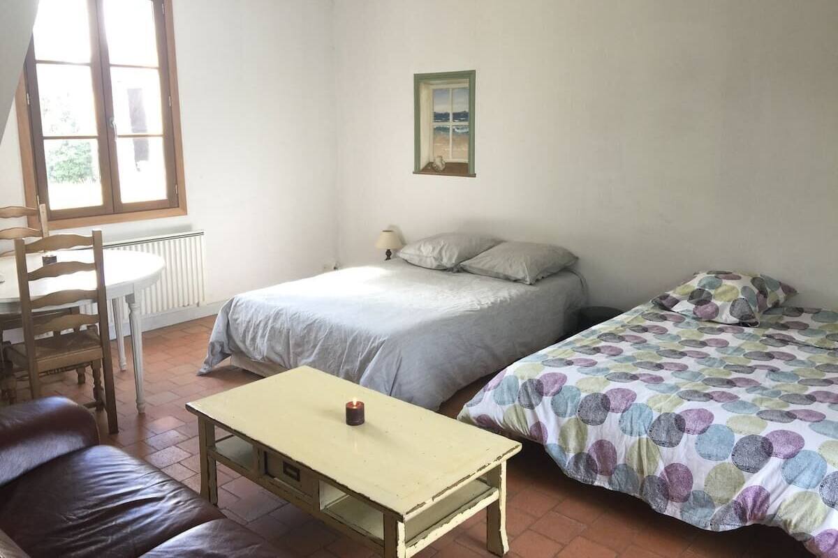 Een slaapkamer met een bed, een tafeltje, een stoel en een raam.