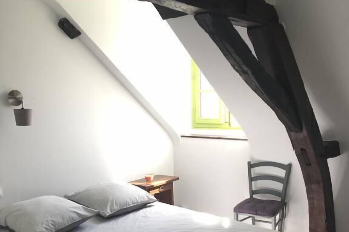 Een slaapkamer met een bed, een stoel, een nachtkastje en een raam.