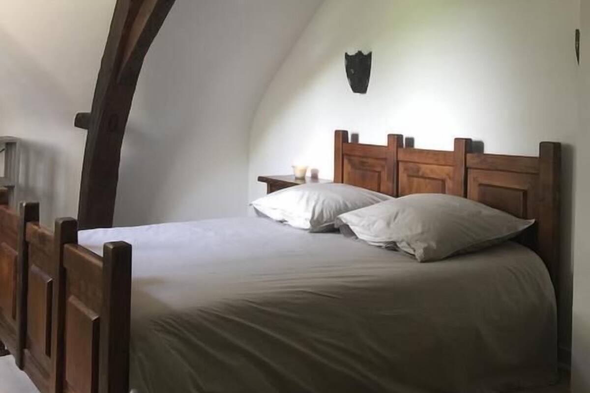 Een slaapkamer met een houten bedframe, witte beddengoed en een schuin plafond met zichtbare balken.