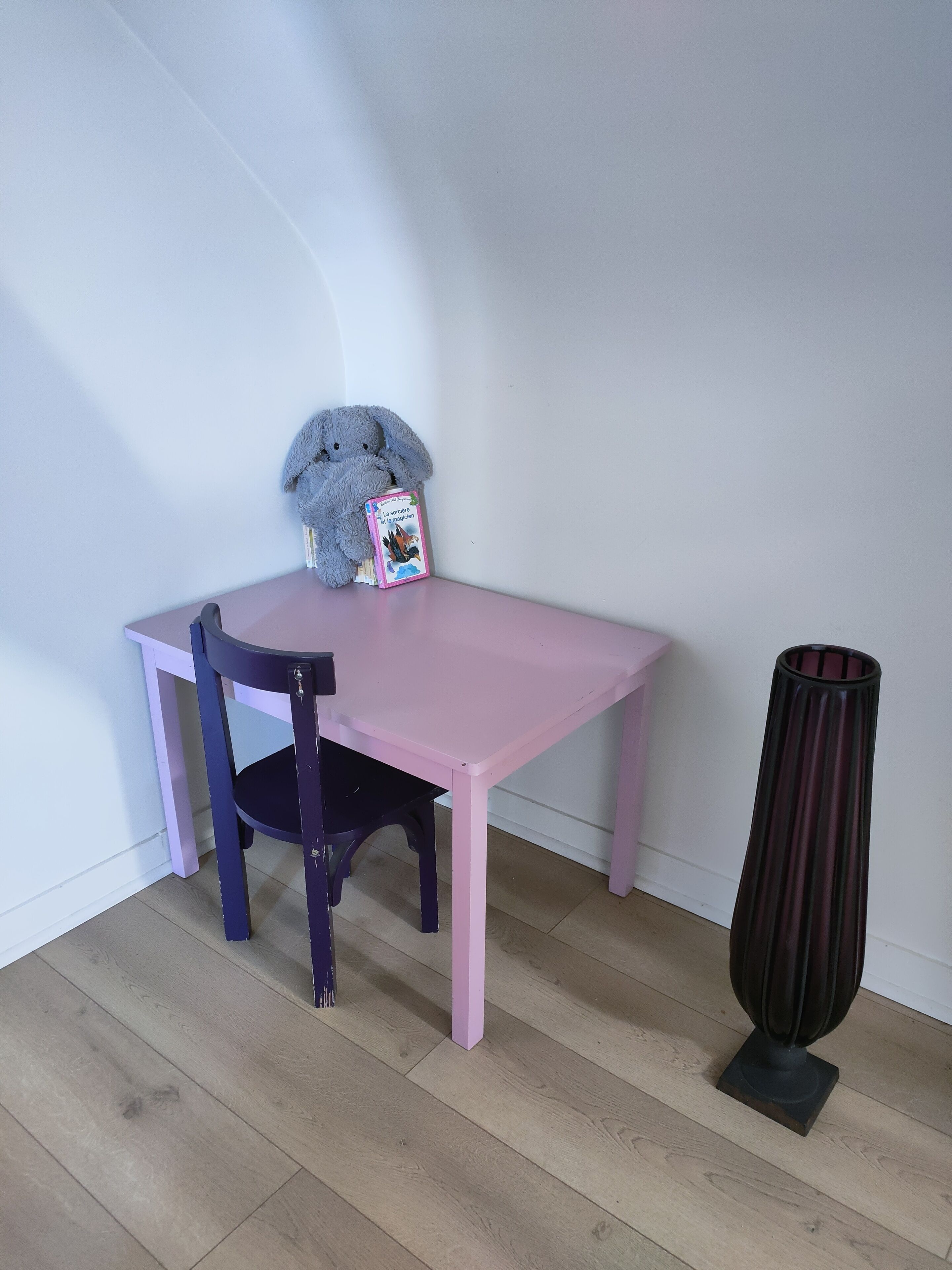 A pink table with a chair, a book, and a tall vase.