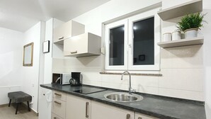 A compact kitchen with white cabinets, a black countertop, a stainless steel sink, and a window above the sink. - Apartments Karla (Bibinje)