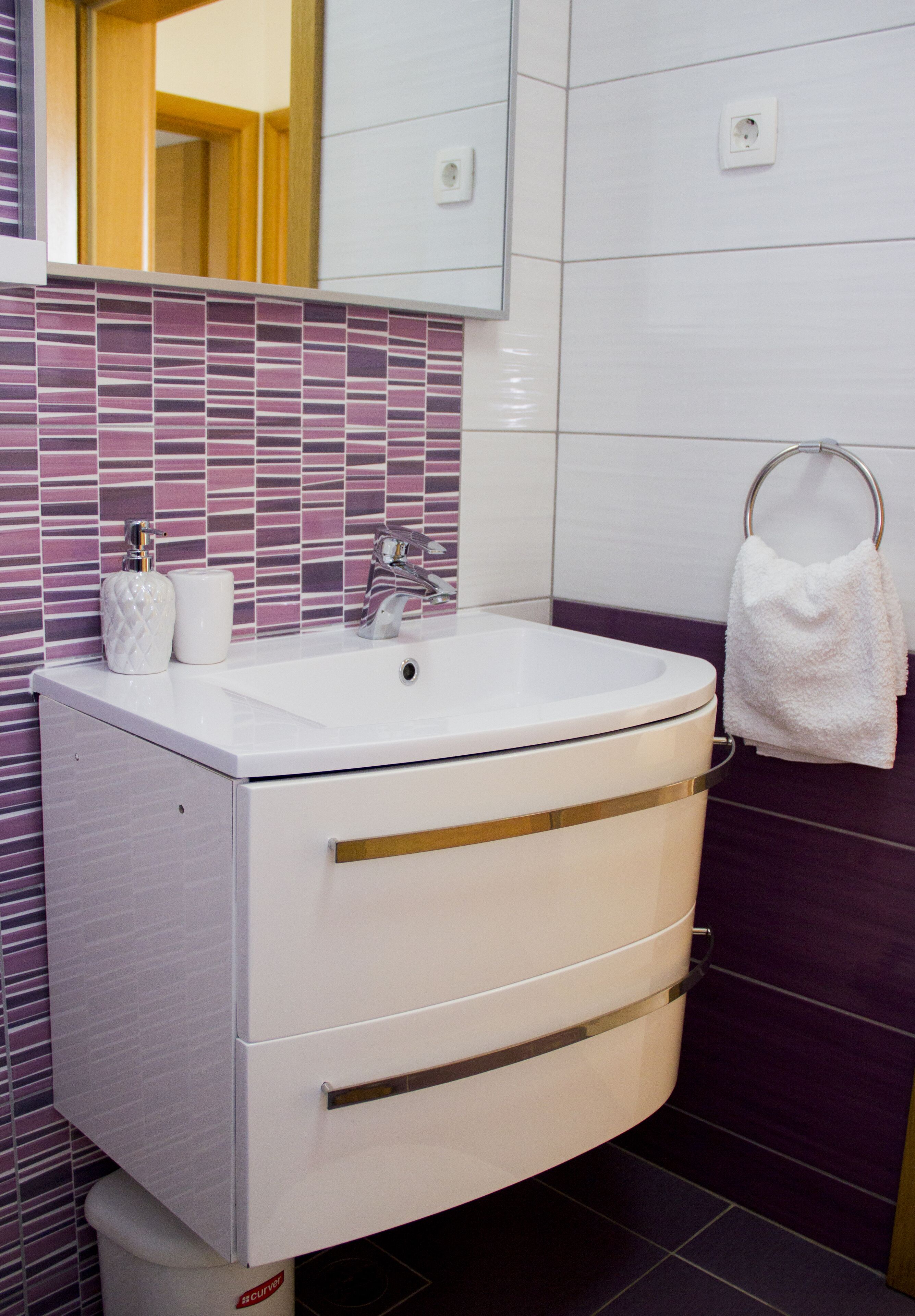 Un baño con un lavamanos blanco, un espejo encima y una pared con azulejos morados.