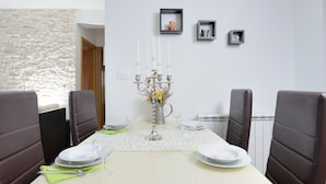 A dining room with a table set for four, chairs, a vase with flowers, and a wall-mounted shelf with decorative items. - Apartments Karla (Bibinje)