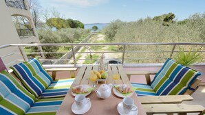 A terrace with striped cushions, a table set with a teapot, cups, and plates with pastries, overlooking a path and greenery. - Apartments Karla (Bibinje)