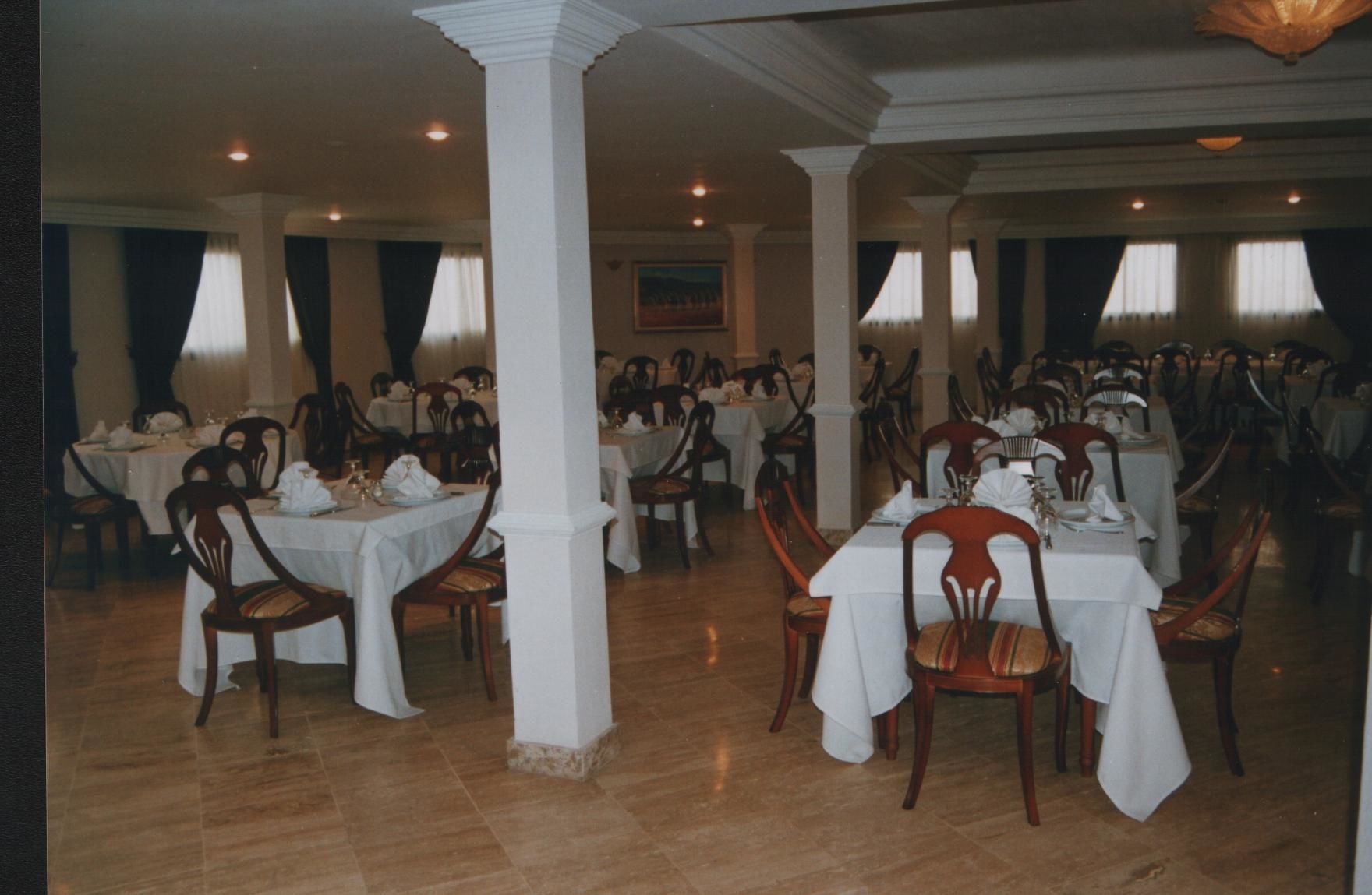 Un vaste espace dédié à la salle à manger, avec de nombreuses tables et chaises, des nappes blanches et des chaises en bois.