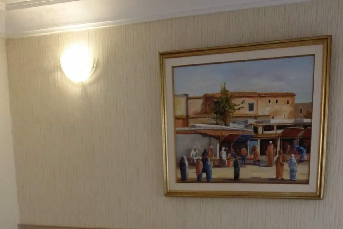 A hotel room with a large bed, a nightstand, a wall-mounted painting, and a light fixture.