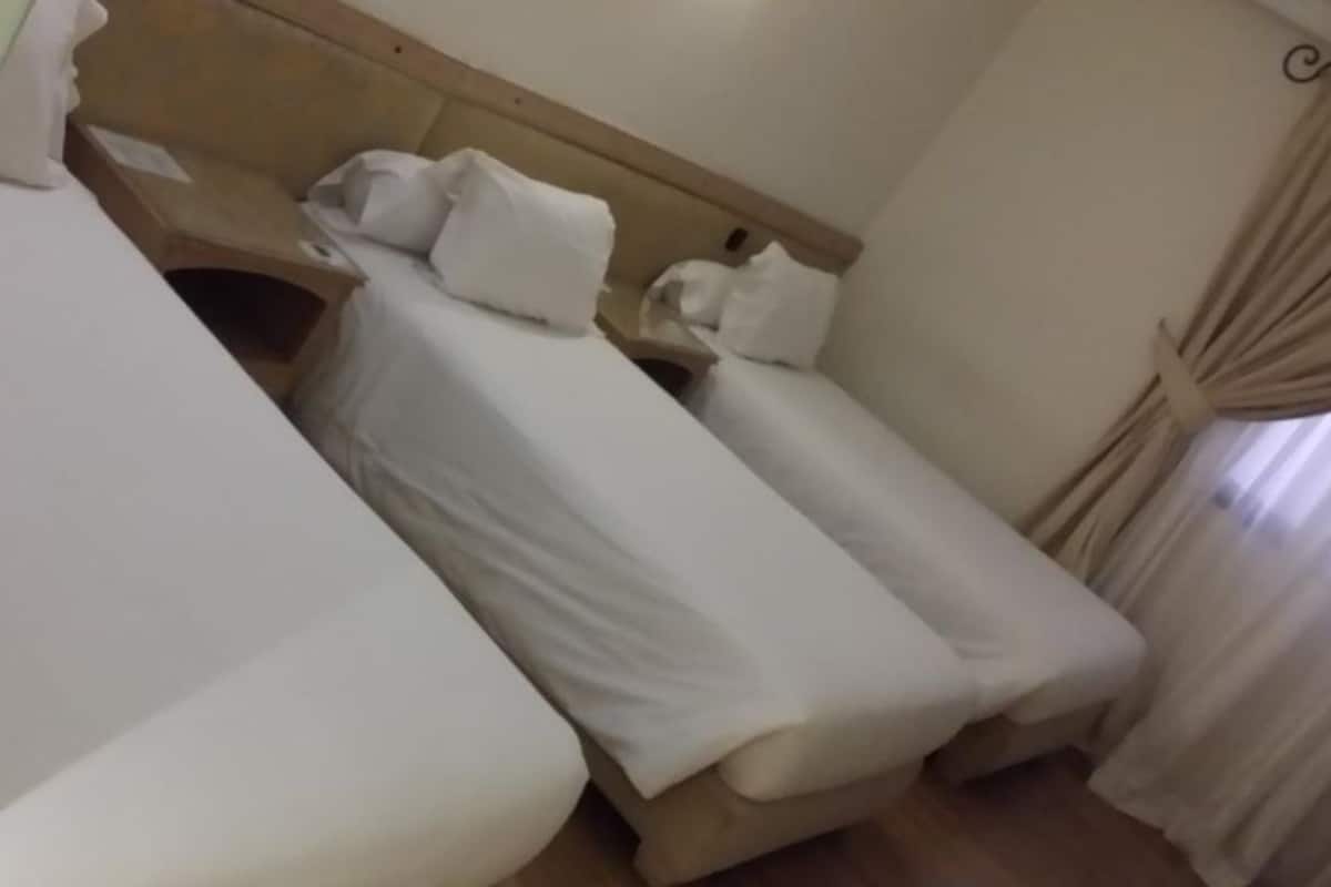 A hotel room with two single beds, a wooden headboard, and a window with curtains.