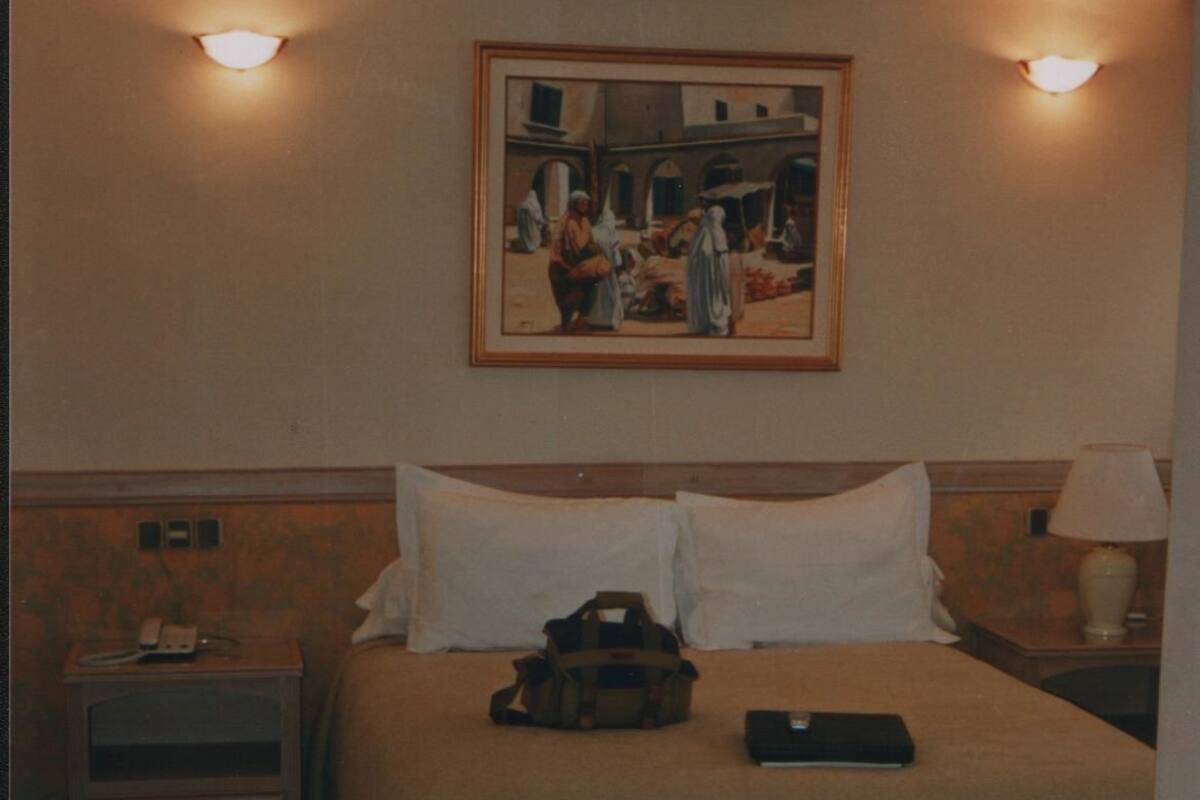 A hotel room with a bed, bedside tables, a lamp, a painting, and a suitcase.