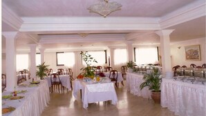 A spacious dining hall with multiple tables, white tablecloths, and potted plants. - Sahara Line Hotel (Laayoune)