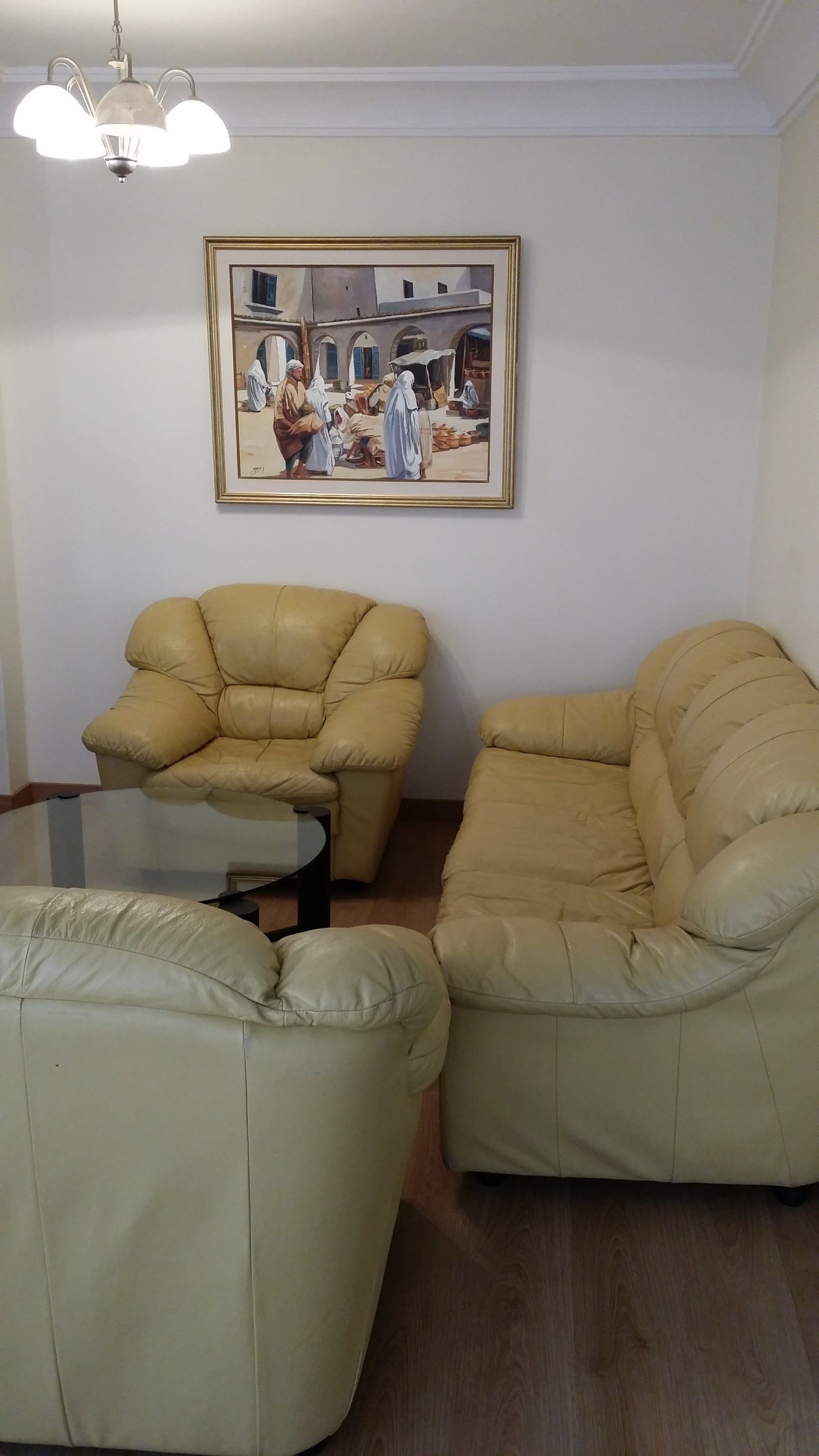 Een woonkamer met twee beige fauteuils, een glazen salontafel en een lijstwerk met een schilderij.