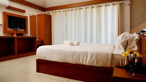 A hotel room with a large bed, a TV mounted on the wall, a wooden desk, and a window with curtains. - Wayanad Ranches Resorts (Vythiri)