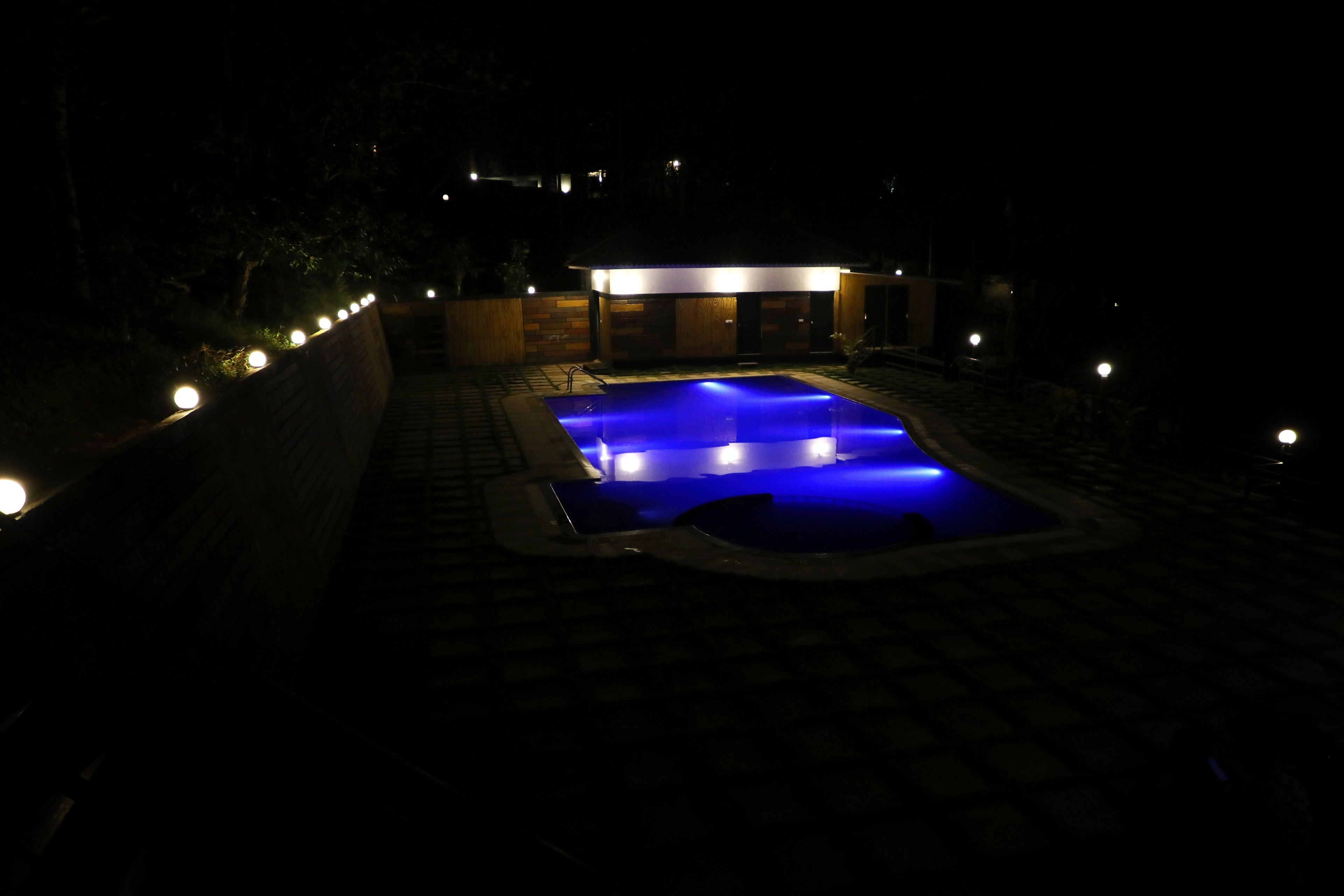Une piscine illuminée la nuit, avec des lumières disposées tout autour et un bâtiment en arrière-plan.
