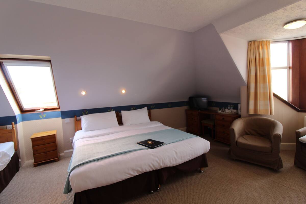 A hotel room with a large bed, a chair, a desk, and a window with curtains.