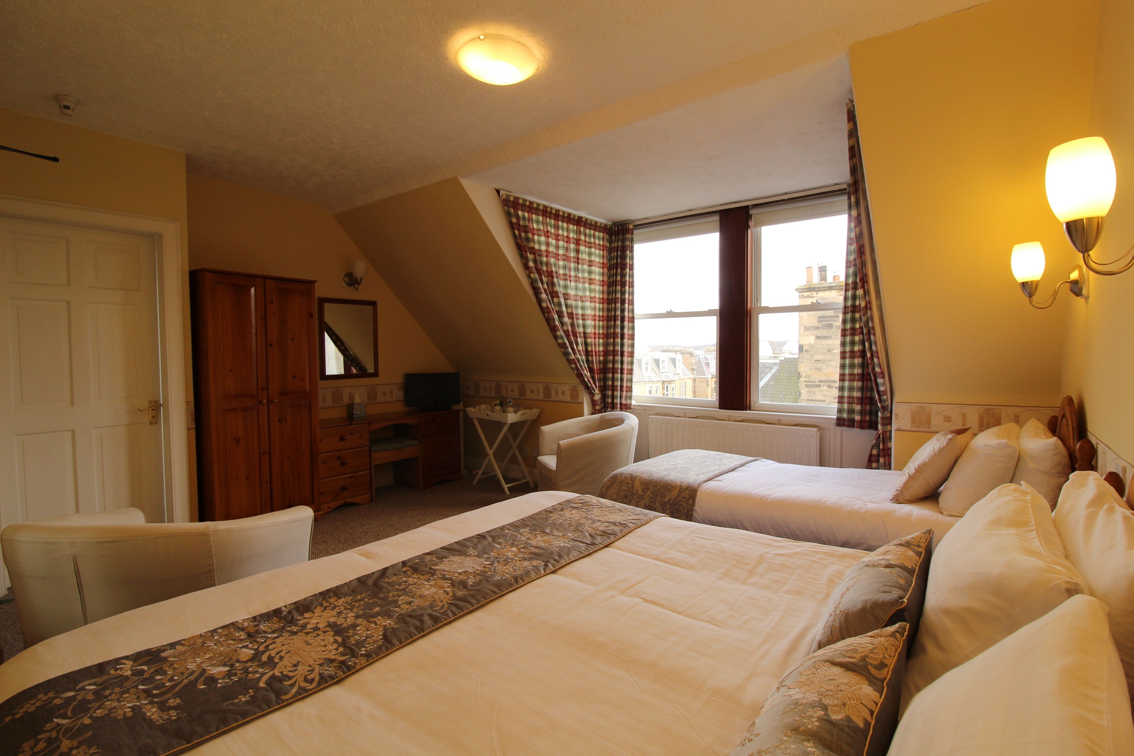 A hotel room with two beds, a desk, a chair, a wardrobe, and a window with curtains.