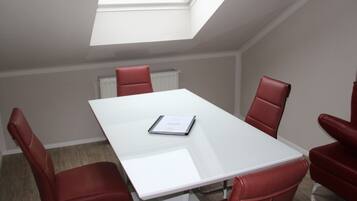 A conference room with a white table and red chairs, a skylight, and a radiator on the wall.