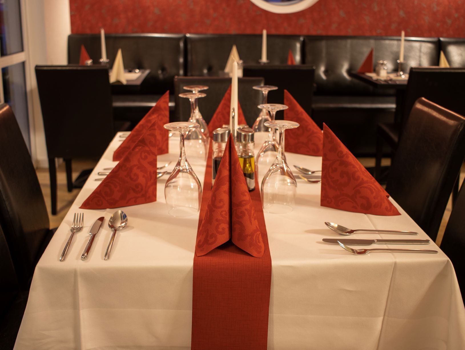 A restaurant table set with wine glasses, cutlery, and a red napkin.
