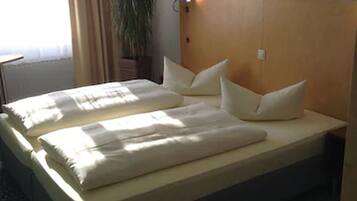 A hotel room with a large bed, a headboard with a light, a potted plant, and a window with curtains.