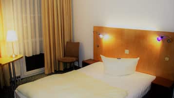 A hotel room with a bed, a chair, a desk with a lamp, and curtains.