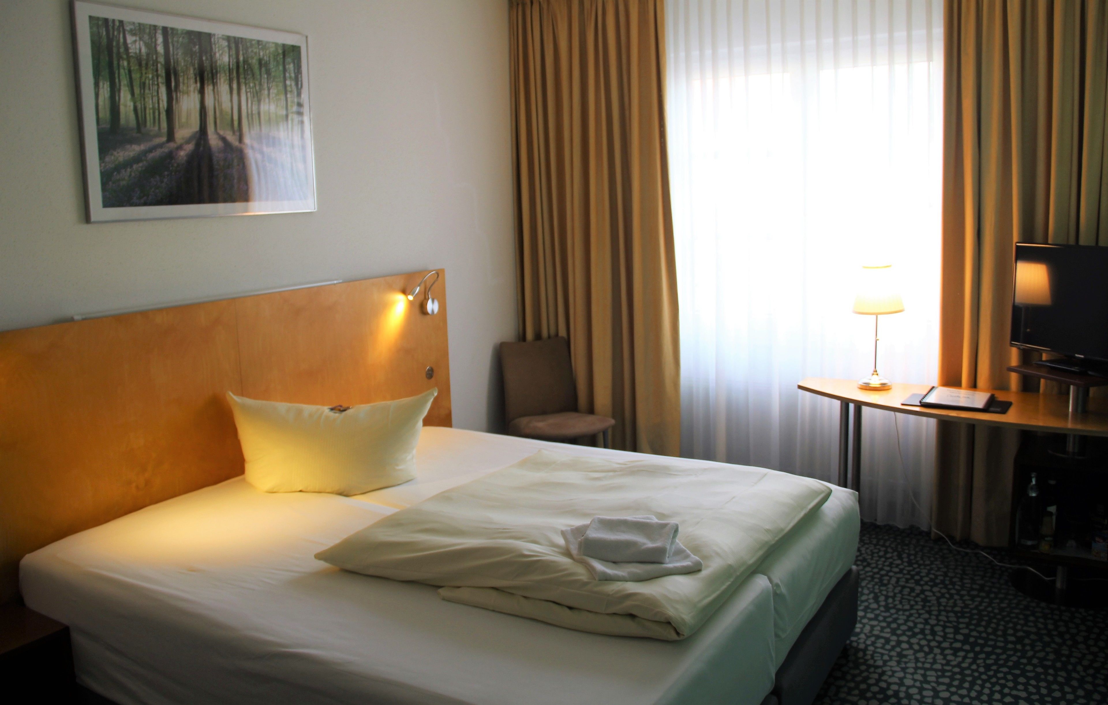 Una habitación de hotel con una cama, una silla, un escritorio con lámpara y un televisor.