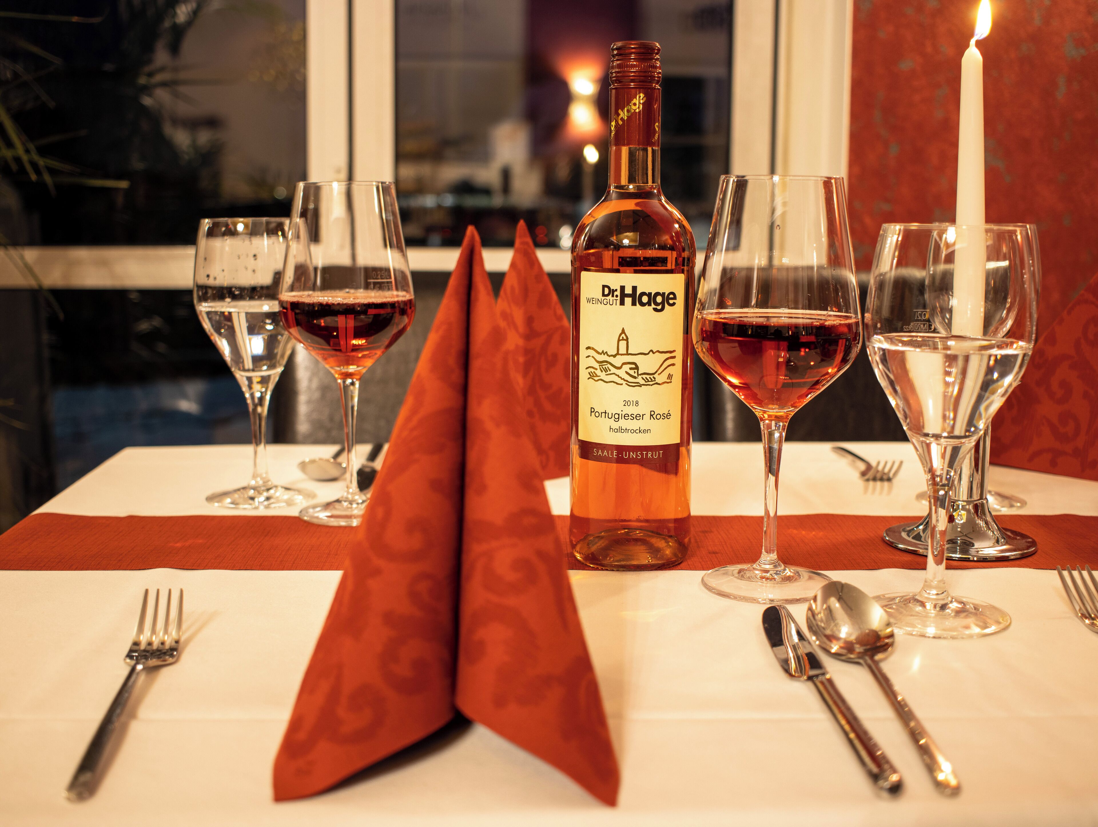 A table set with wine glasses, a bottle of wine, and cutlery.