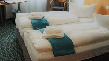 Une chambre d’hôtel avec deux lits, chacun agrémenté de draps blancs soigneusement pliés et de coussins décoratifs de couleur turquoise.