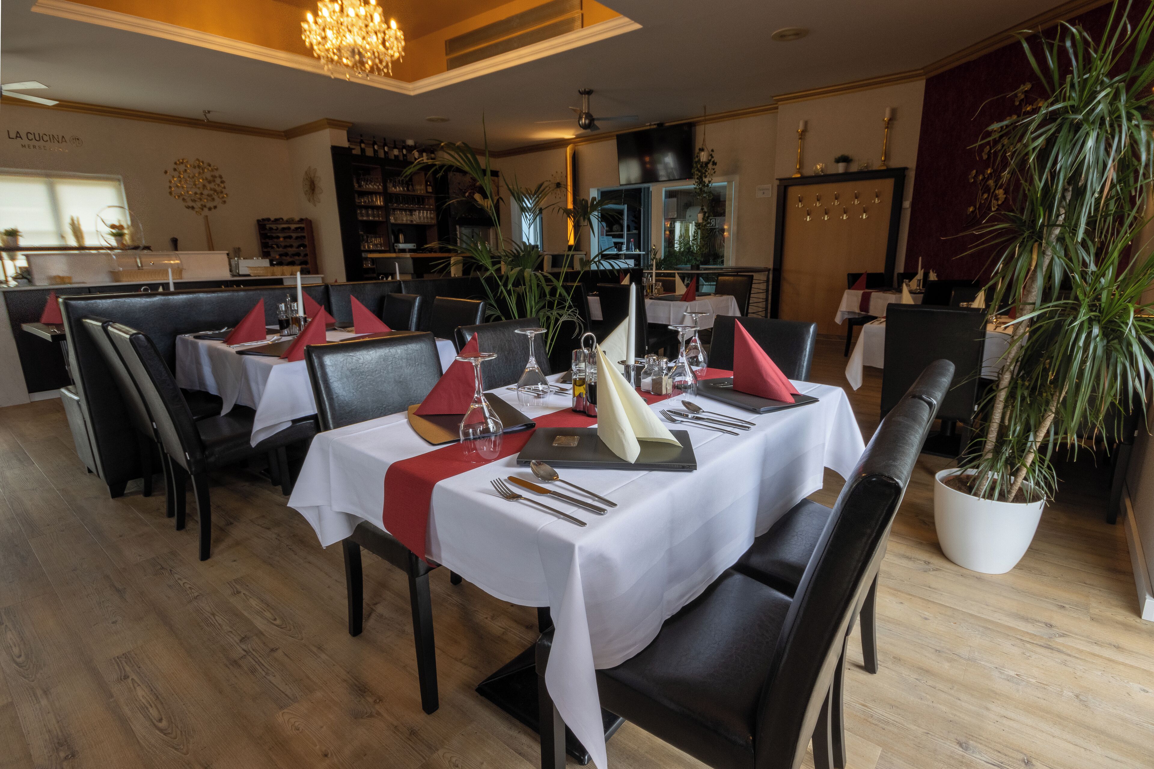 A restaurant with tables set for dining, featuring white tablecloths and red napkins.