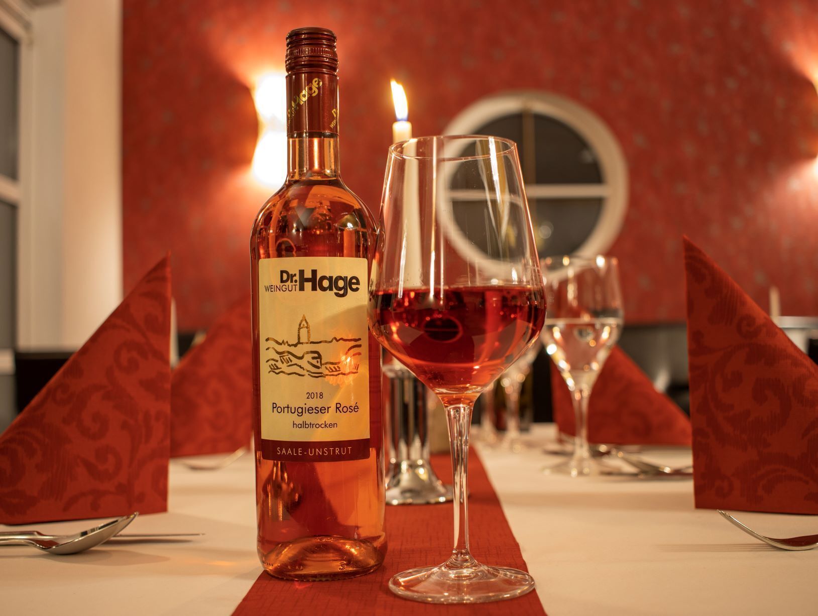 A bottle of Dr. Hage wine and a glass of red wine on a table with a red tablecloth.