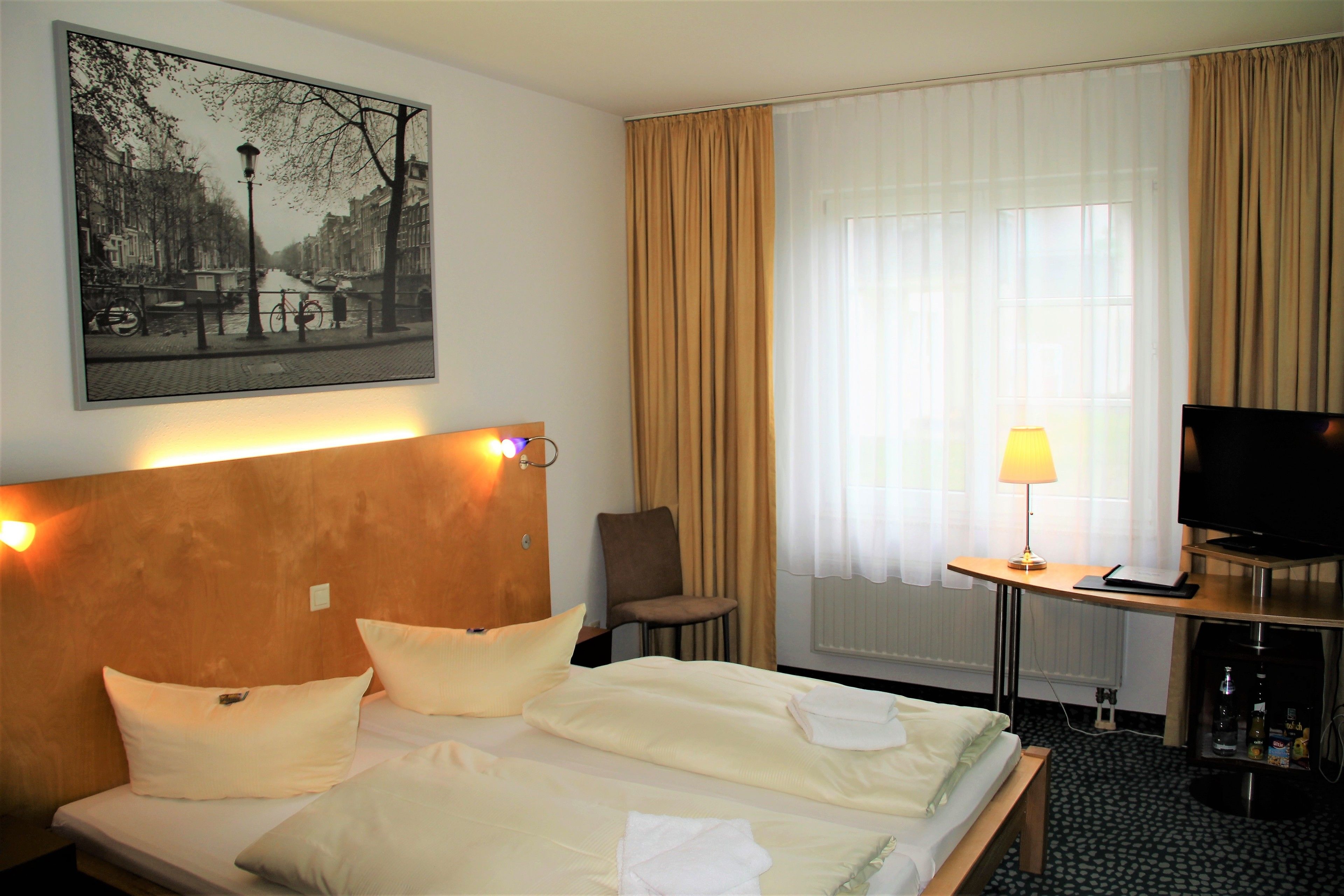 Een hotelkamer met een bed, een stoel, een televisie, een lamp en een schilderij aan de muur.