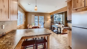 A spacious kitchen with wooden cabinets, a granite countertop, and a dining area with a table and chairs. - Mountainside 753 3 Bedroom Home by RedAwning (Frisco)