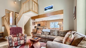 A spacious living area with a high wooden staircase, a cozy sofa set, and a kitchen in the background. - Mountainside 753 3 Bedroom Home by RedAwning (Frisco)