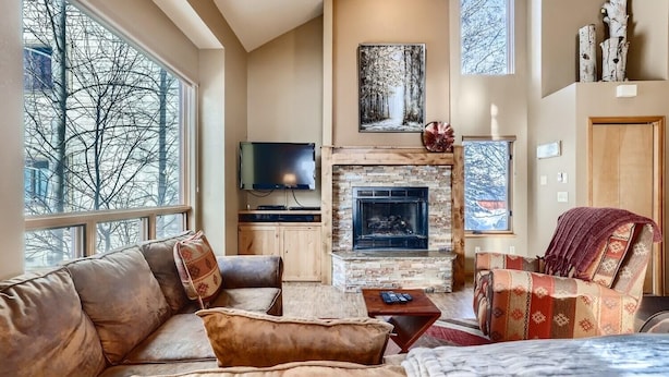 A cozy living room with a fireplace, leather sofa, and a television. - Mountainside 753 3 Bedroom Home by RedAwning (Frisco)