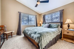 A bedroom with a bed, two windows with curtains, a desk, a chair, a nightstand with a lamp, and a ceiling fan. - Mountainside 753 3 Bedroom Home by RedAwning (Frisco)