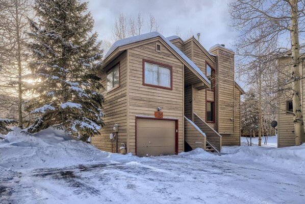 A two-story wooden house with a garage, surrounded by snow-covered trees. - Mountainside 753 3 Bedroom Home by RedAwning (Frisco)