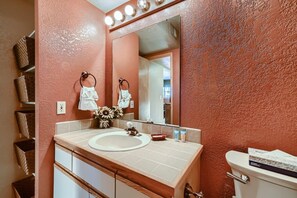 A bathroom with a pink textured wall, a white sink, a mirror, and a toilet. - Mountainside 753 3 Bedroom Home by RedAwning (Frisco)