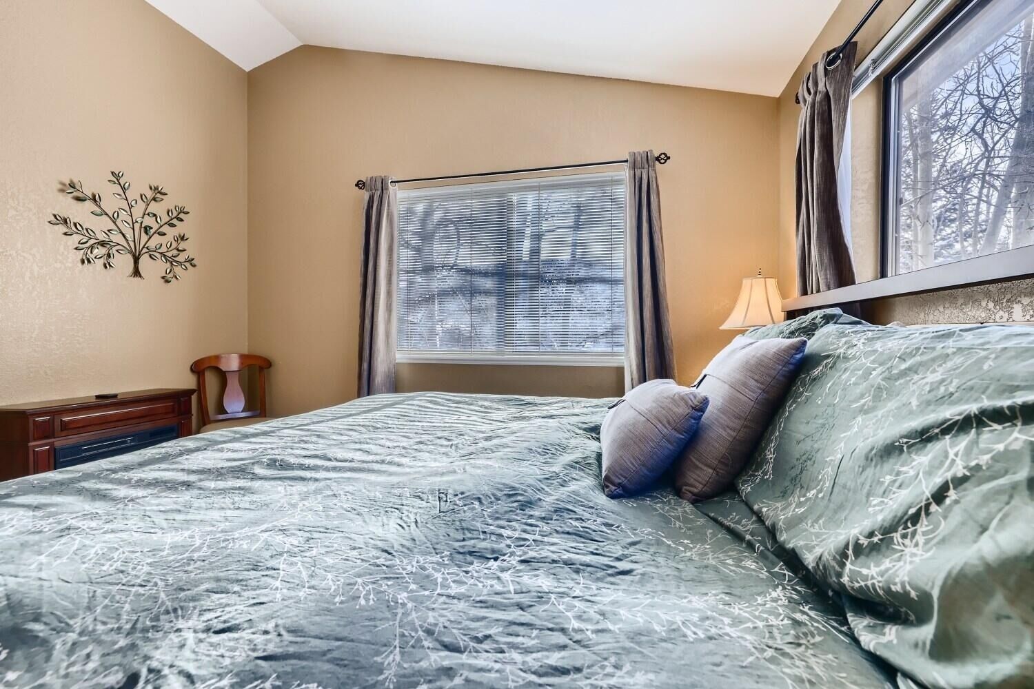 A bedroom with a bed, a nightstand, a lamp, a window with blinds, and a wall decoration.