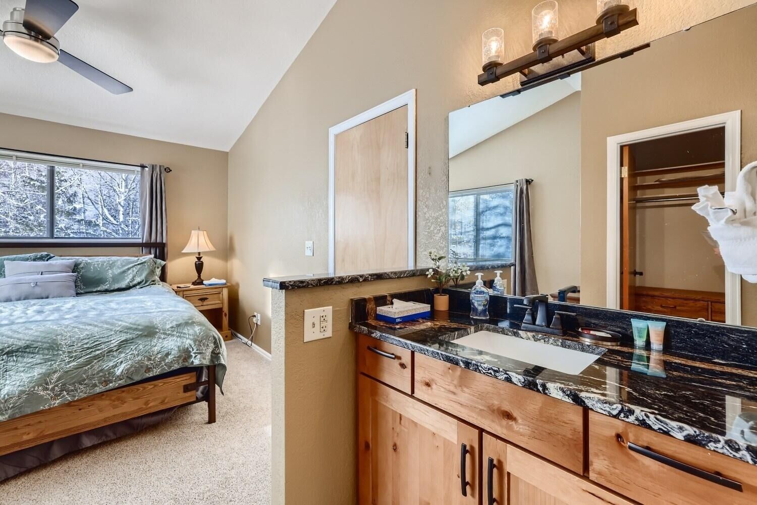 A bedroom with a bed, bedside table, lamp, and a large window.