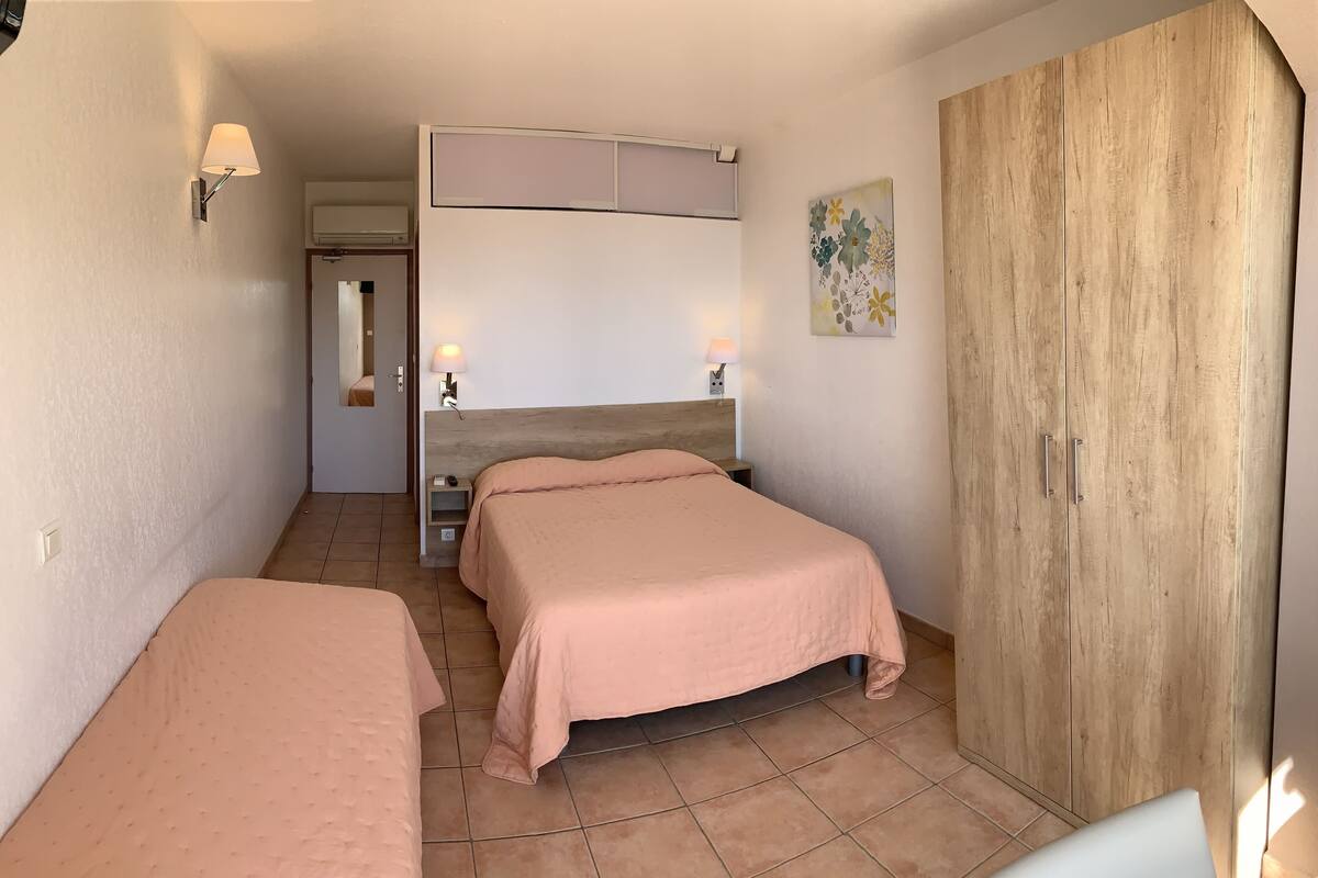 Une chambre avec deux lits, une armoire en bois, un climatiseur fixé au mur et deux lampes de chevet.