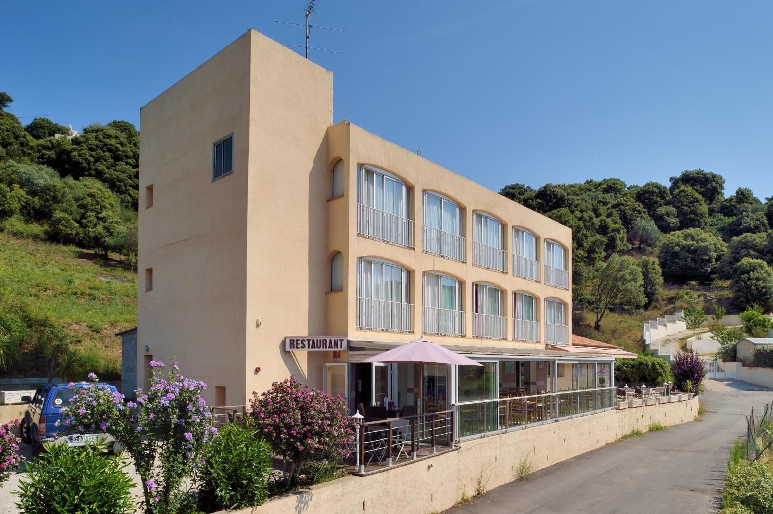 A two-story building with a 'RESTAURANT' sign, outdoor seating, and a hillside backdrop.