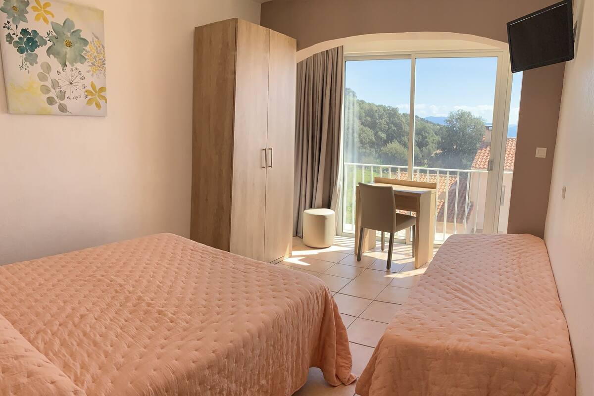 Une chambre d’hôtel avec deux lits, un bureau et un balcon offrant une vue.