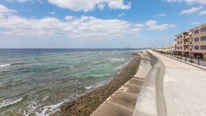 A coastal promenade with a clear view of the sea, a concrete walkway, and a modern building with balconies. - Villa Del Oro Oceanside (Chatan)
