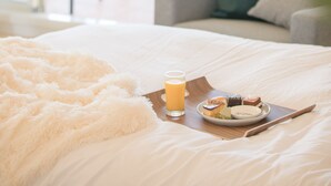 A hotel room with a bed, a breakfast tray with pastries and a glass of orange juice, and a view of the outdoor seating area through large windows. - Villa Del Oro Oceanside (Chatan)