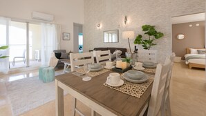 A dining area with a wooden table set for four, surrounded by white chairs. A large mirror and a wall-mounted lamp are visible. - Villa Del Oro Oceanside (Chatan)