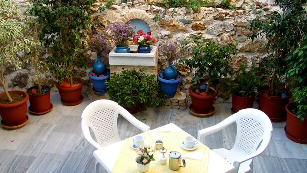 Une terrasse extérieure avec des murs en pierre, des plantes en pot et une table dressée pour deux personnes, avec des chaises.