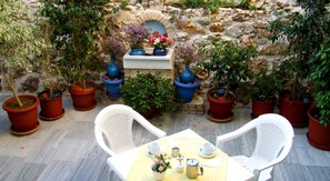 Une terrasse extérieure avec des murs en pierre, des plantes en pot et une table dressée pour deux personnes, avec des chaises.